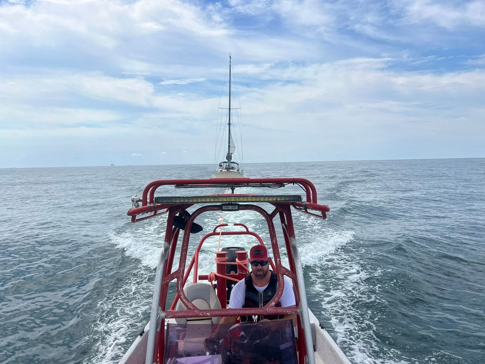 A TowBoatUS Sabine Lake rescue boat with red and white hull and a person aboard towing a sailboat on the open water.