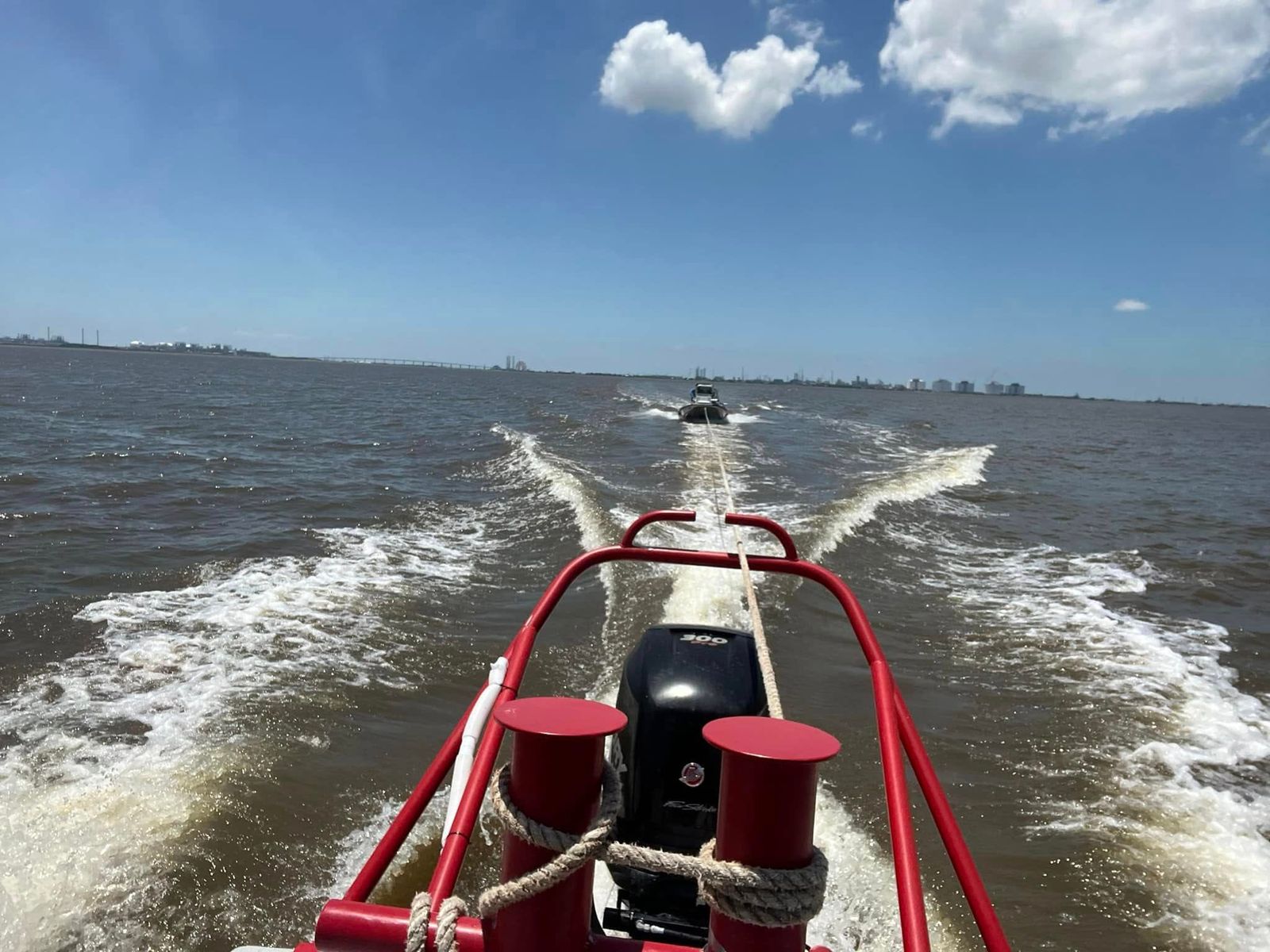 A TowBoatUS rescue boat with red railings powers across Sabine Lake, towing another vessel through choppy water.