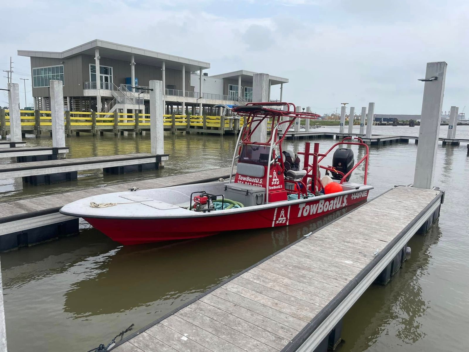 A red TowBoatUS rescue vessel with twin outboard motors docked at the Sabine Lake facility.